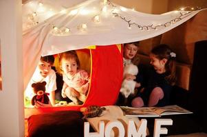 spelende kinderen met kitty in tent 's nachts thuis. hygge stemming. foto