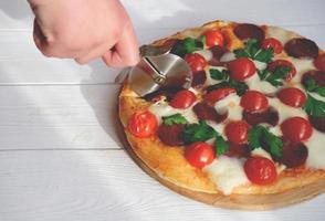 menselijke hand met pizzasnijder gesneden pizza in de keuken. foto