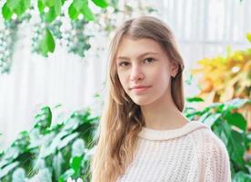 portret van een tienermeisje in haar huis in huis tuinkamer. groene planten op een achtergrond. rustige zelfverzekerde tiener die naar de camera kijkt foto