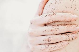 close-up van een vrouw die haar arm vasthoudt en koffie body scrub toepast. thuis kuuroord. me-time en ontspannende schoonheidsbehandeling. selectieve focus foto