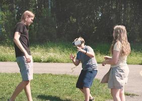 tieners die een virtual reality-headset gebruiken en buiten plezier hebben. twee blanke jongens en blond krullend meisje die virtueel spel spelen in een zomerpark foto