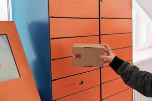 hand met een doos of pakket naast een zelfbedieningspostterminal. contactloze levering, automatische verzendmachine foto