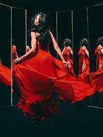 portret van mooie brunette vrouw in rode schoenen en jurk die zich omdraait en danst in de buurt van de spiegels foto