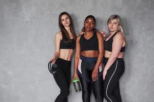 doos met sportief eten en koptelefoon in handen. groep multi-etnische vrouwen die in de studio staan tegen een grijze achtergrond foto