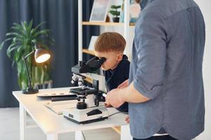 jongen zit met Microscoop op school met leraar. opvatting van onderwijs foto