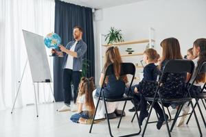 aardrijkskunde les. met wereldbol in handen. groep kinderen studenten in de klas op school met leraar foto