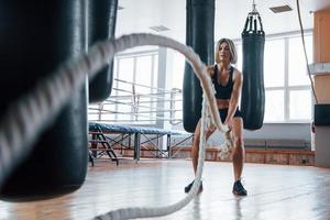 ruime kamer. blonde sportvrouw heeft oefening met touwen in de sportschool. sterke vrouw foto