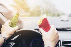 man rijdt auto terwijl hij frietjes en bier eet foto