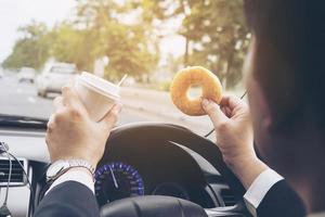 man die donuts eet met koffie tijdens het autorijden - multitasking onveilig rijconcept foto