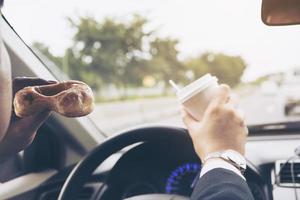 man die donuts eet met koffie tijdens het autorijden - multitasking onveilig rijconcept foto