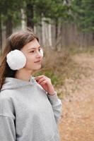 openluchtportret van tienermeisje die witte oorbeschermers dragen. meisje wandelen in het bos. tiener op zoek opzij. alleen wandelen en volgen. lokaal reisconcept foto