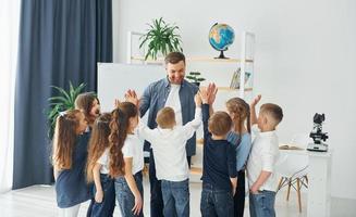 staan en high fives geven. groep kinderen studenten in de klas op school met leraar foto