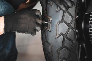 rijder gebruikt een bandenplugset en probeert een gat in de zijwand van de band te repareren, repareer een lekke motorfietsband in de garage. motorfiets onderhoud en reparatie concept foto