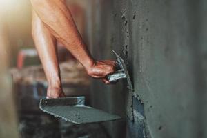 close-up hand van werknemer die cement aan de muur pleistert voor het bouwen van een huis foto