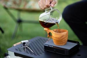 jonge man gieten koffie in beker, ochtendontbijt op open lucht. reiziger die voor het eerst kampeert, nieuwe ervaring om uit te rusten met tent. natuur, vrije tijd, geen haast, vrede en rust concept foto