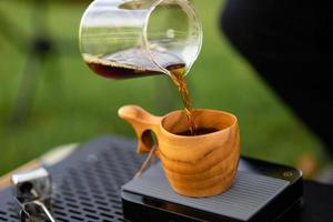 jonge man gieten koffie in beker, ochtendontbijt op open lucht. reiziger die voor het eerst kampeert, nieuwe ervaring om uit te rusten met tent. natuur, vrije tijd, geen haast, vrede en rust concept foto