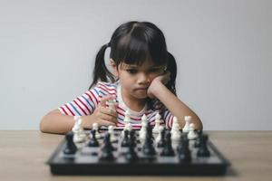 Aziatisch klein meisje schaakt thuis. Een spelletje schaak foto