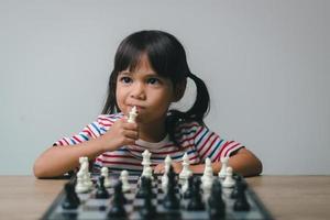 Aziatisch klein meisje schaakt thuis. Een spelletje schaak foto