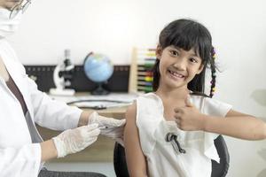 vaccinatie concept. vrouwelijke arts die schattig klein meisje in kliniek vaccineert foto
