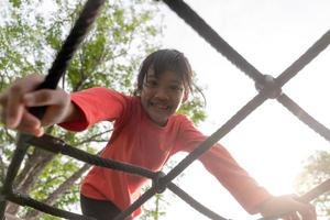 zomer, kinderjaren, vrije tijd en mensenconcept - gelukkig meisje op het klimrek van de kinderspeelplaats foto