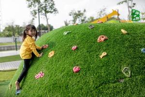 kind spelen op buitenspeeltuin. kinderen spelen op school of kleuterschool. actieve jongen op kleurrijke glijbaan en schommel. gezonde zomeractiviteit voor kinderen. klein meisje buitenshuis klimmen. foto