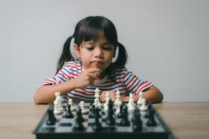 Aziatisch klein meisje schaakt thuis. Een spelletje schaak foto