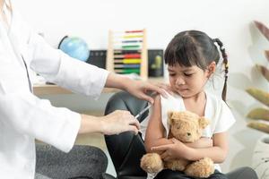 vaccinatie concept. vrouwelijke arts die schattig klein meisje in kliniek vaccineert foto