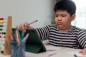 schattig Aziatisch kind dat klassikaal online leert met videogesprek vanaf tablet thuis .social distancing concept foto