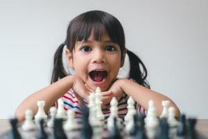 Aziatisch klein meisje schaakt thuis. Een spelletje schaak foto