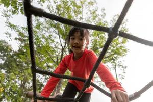 zomer, kinderjaren, vrije tijd en mensenconcept - gelukkig meisje op het klimrek van de kinderspeelplaats foto