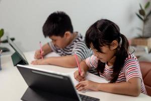 Aziatische jongens en meisjes genieten van online leren door thuis aantekeningen te maken en tablets te gebruiken. foto