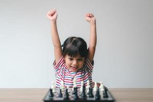 Aziatisch klein meisje schaakt thuis. Een spelletje schaak foto