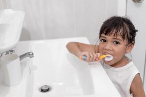 klein schattig babymeisje dat haar tanden schoonmaakt met een tandenborstel in de badkamer foto