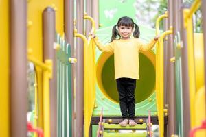 kind spelen op buitenspeeltuin. kinderen spelen op school of kleuterschool. actieve jongen op kleurrijke glijbaan en schommel. gezonde zomeractiviteit voor kinderen. klein meisje buitenshuis klimmen. foto