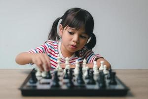 Aziatisch klein meisje schaakt thuis. Een spelletje schaak foto
