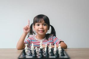 Aziatisch klein meisje schaakt thuis. Een spelletje schaak foto