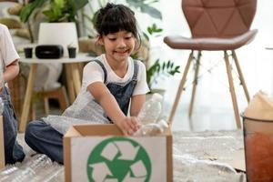 lachende kinderen die plezier hebben terwijl ze plastic flessen en papier scheiden in een prullenbak foto