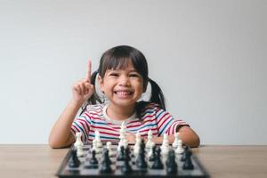 Aziatisch klein meisje schaakt thuis. Een spelletje schaak foto