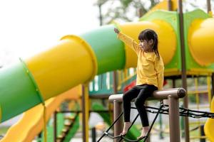 Aziatisch kindmeisje dat op de speelplaats in het openluchtpark speelt. Gelukkig moment en goede emotie foto