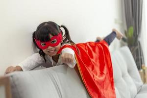 kindmeisje in een superheldenkostuum met masker en rode mantel thuis foto