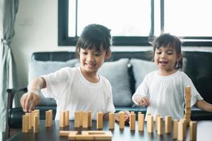 twee gelukkige broers en zussen spelen thuis vreugdevol een spel met houten blokken foto