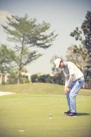 golfspeler bij de putting green die de bal in een hole.vintage color slaat foto