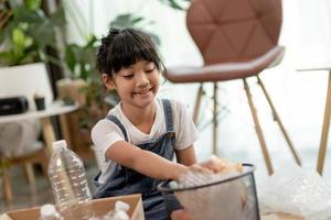 lachende kinderen die plezier hebben terwijl ze plastic flessen en papier scheiden in een prullenbak foto