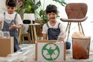 lachende kinderen die plezier hebben terwijl ze plastic flessen en papier scheiden in een prullenbak foto