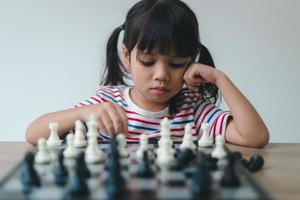 Aziatisch klein meisje schaakt thuis. Een spelletje schaak foto