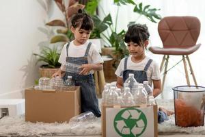 lachende kinderen die plezier hebben terwijl ze plastic flessen en papier scheiden in een prullenbak foto