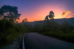 zonsondergangpanorama met lege weg in bos met berg foto