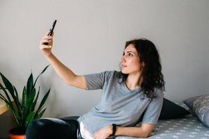 een jonge brunette vrouw rust thuis en praat op een smartphone foto