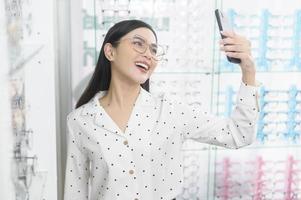 jonge vrouwelijke klant die een bril probeert en een selfie neemt in optisch centrum, oogzorgconcept. foto