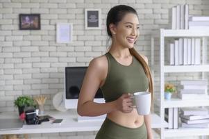 jonge fitnessvrouw in sportkleding met een kopje koffie na het sporten thuis, gezond en levensstijl. foto